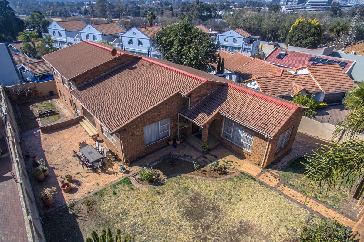 Aerial view of a brick-faced residential house featuring a tiled roof, paved patio area, and a private garden in a suburban setting.