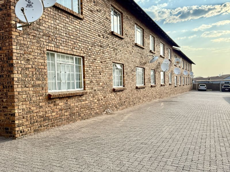 Exterior view of a multi-story apartment building featuring a face brick facade, paved driveway, and multiple satellite dish installations.