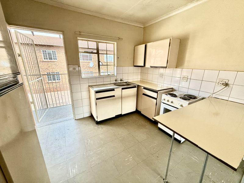 A dated kitchen featuring original cabinetry, a freestanding stove, tiled splashbacks, and direct access to an exterior balcony area.