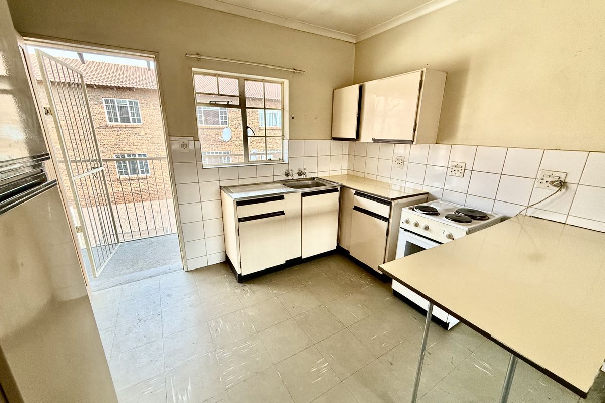 A dated kitchen featuring original cabinetry, a freestanding stove, tiled splashbacks, and direct access to an exterior balcony area.