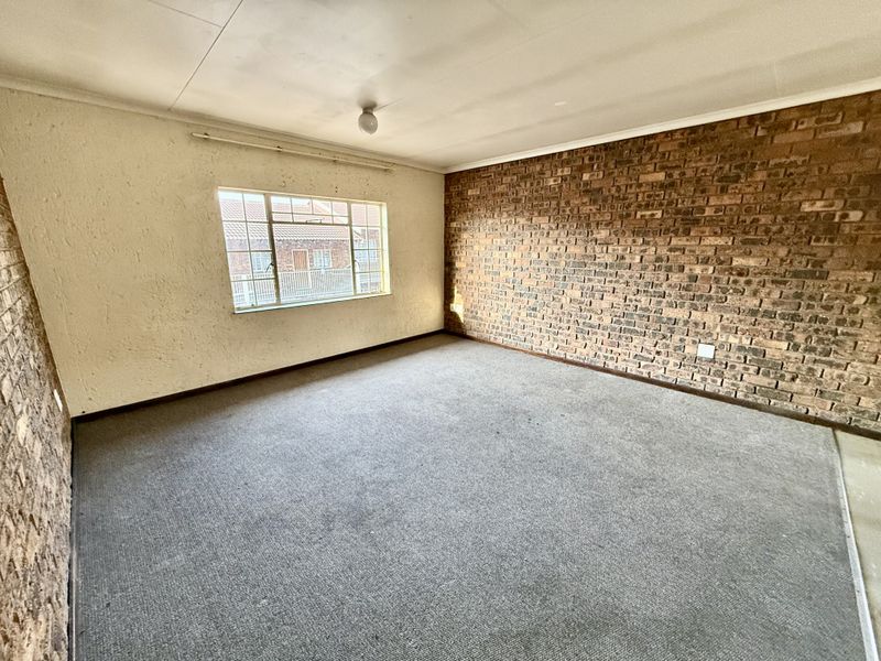 An empty bedroom featuring an exposed brick wall, carpeted flooring, and a steel-framed window, offering a blank canvas for renovation.