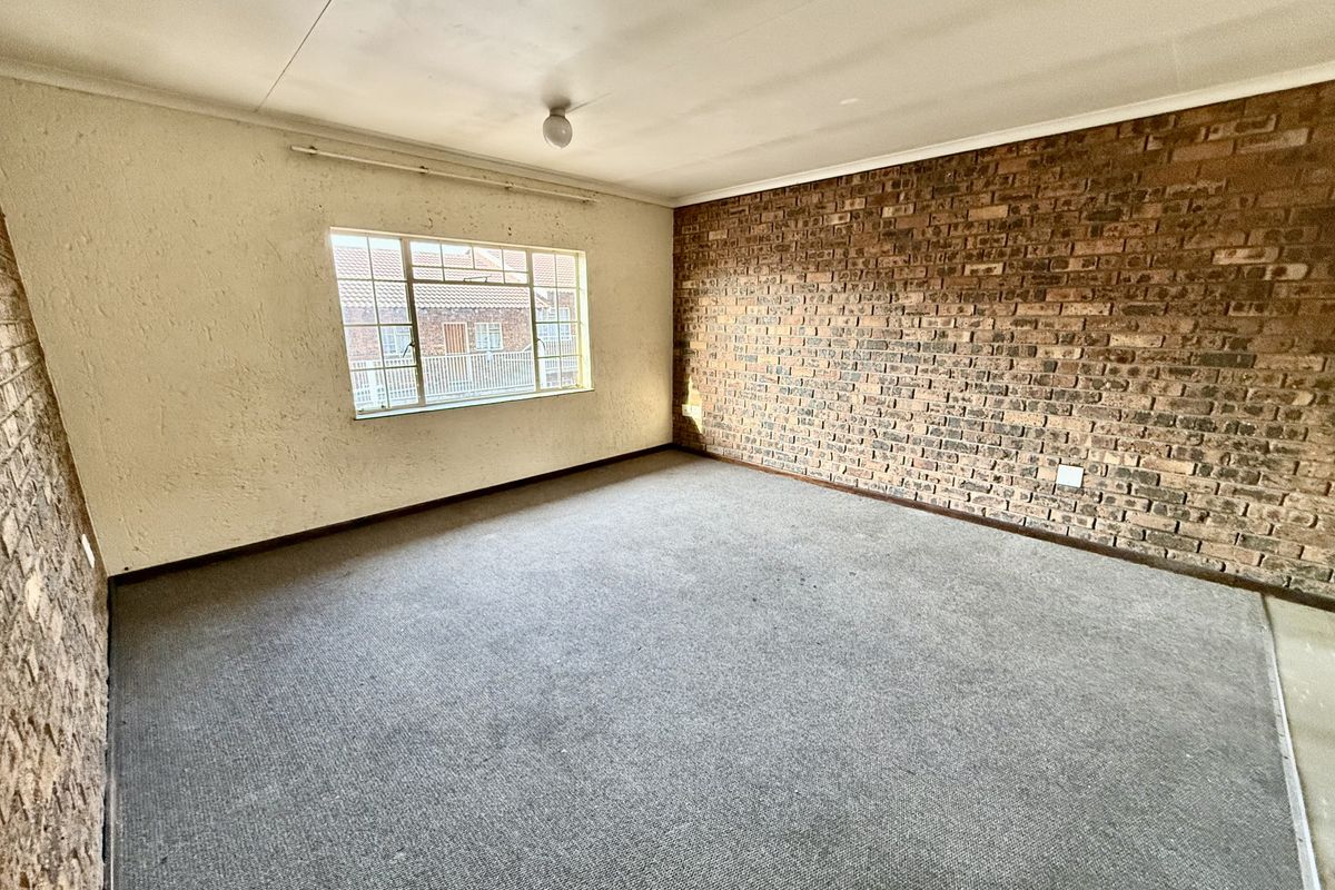 An empty bedroom featuring an exposed brick wall, carpeted flooring, and a steel-framed window, offering a blank canvas for renovation.