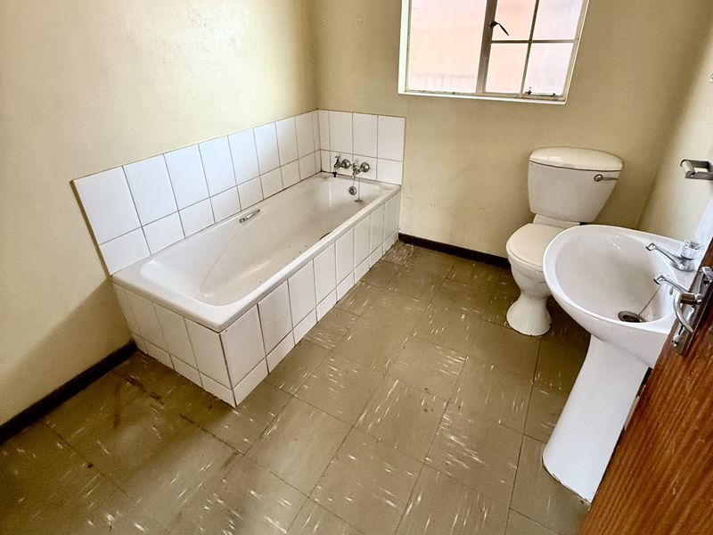 A dated bathroom featuring a standard bathtub, pedestal basin, and toilet, with original floor tiling and a steel-framed window.