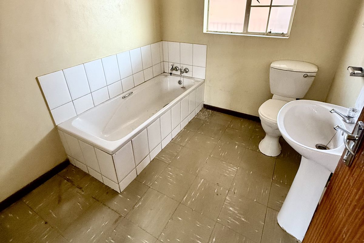 A dated bathroom featuring a standard bathtub, pedestal basin, and toilet, with original floor tiling and a steel-framed window.