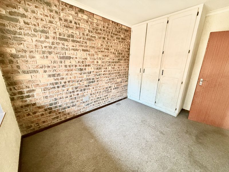 A vacant bedroom featuring an exposed brick accent wall, built-in wardrobe storage, and carpeted flooring, offering a blank canvas for renovation.