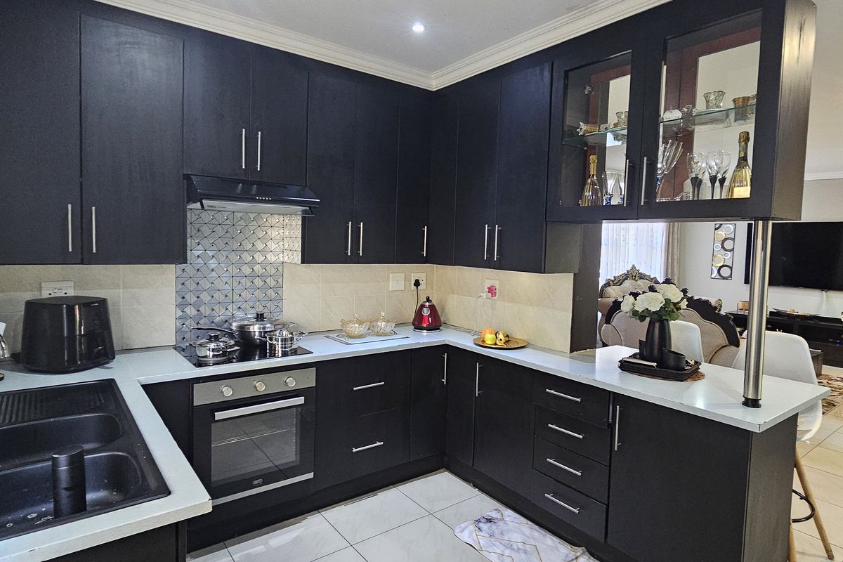 Modern kitchen featuring dark cabinetry, integrated appliances, a tiled backsplash, and a breakfast counter overlooking the adjacent living area.