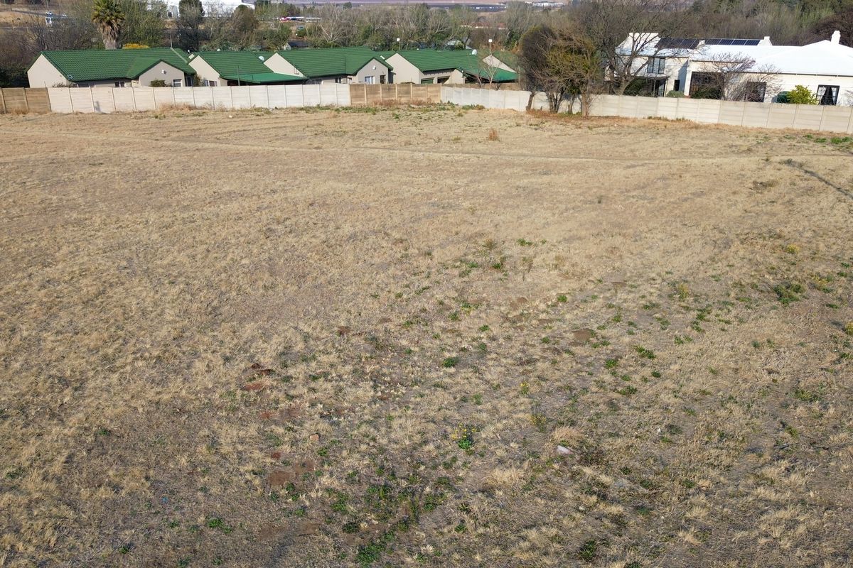 An elevated aerial view of a vacant residential plot featuring dry grass and a perimeter precast concrete boundary wall.