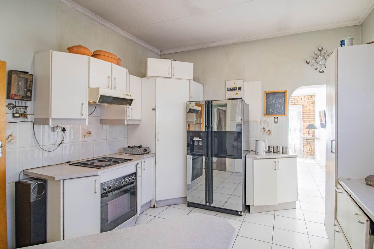 A functional kitchen featuring white built-in cabinetry, an electric hob, oven, extractor fan, and tiled flooring with a neutral aesthetic.