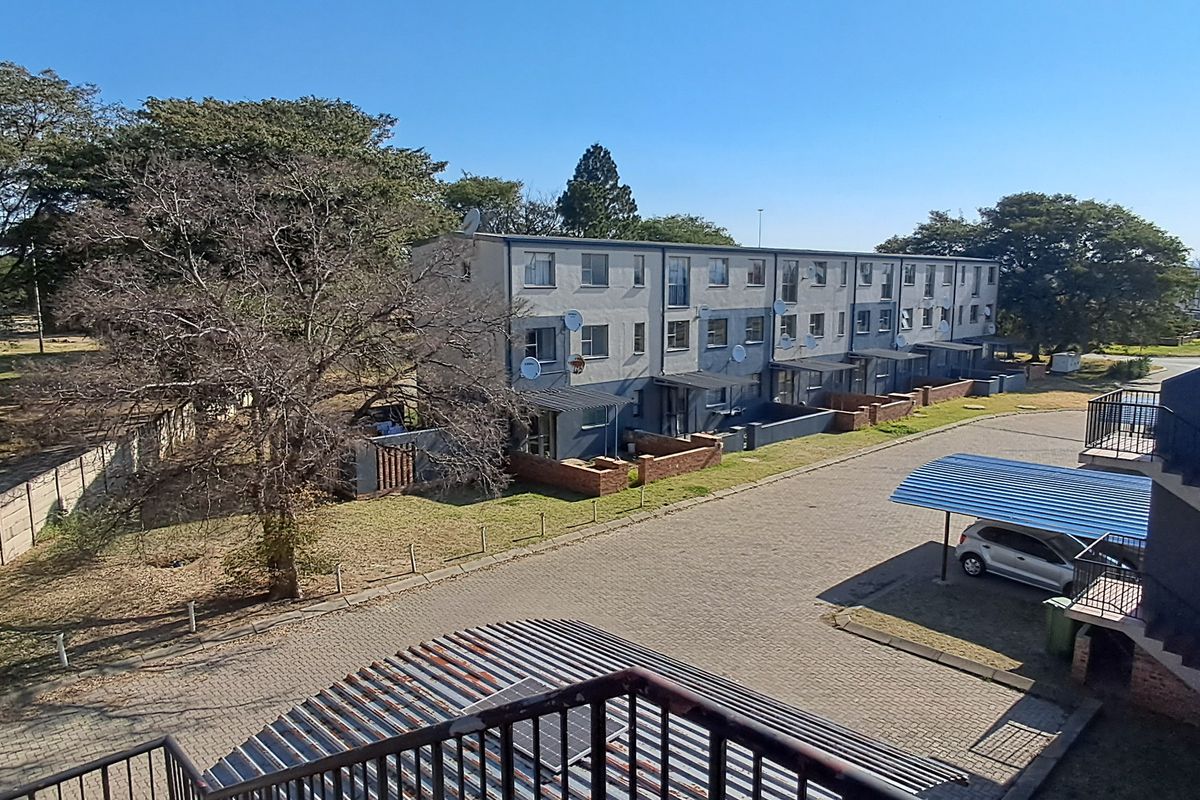 Elevated view of the residential complex grounds, featuring paved parking areas, covered carports, and surrounding landscaped garden space.