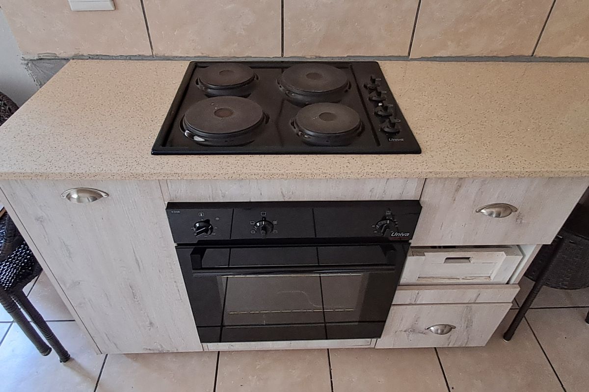 A compact kitchen section featuring a built-in electric oven and hob set into a light wood-grain cabinet with a stone-look countertop.