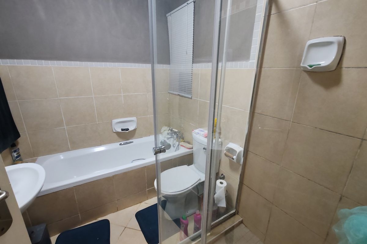 A functional bathroom featuring a bathtub, separate shower enclosure, toilet, and pedestal basin with neutral ceramic wall and floor tiling.