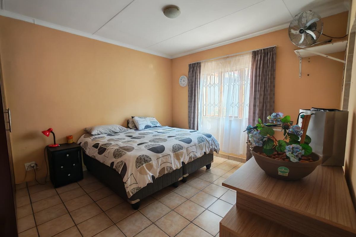 A bedroom featuring tiled flooring, a wall-mounted fan, and security gates on the window. The room requires cosmetic updates to improve its overall condition.