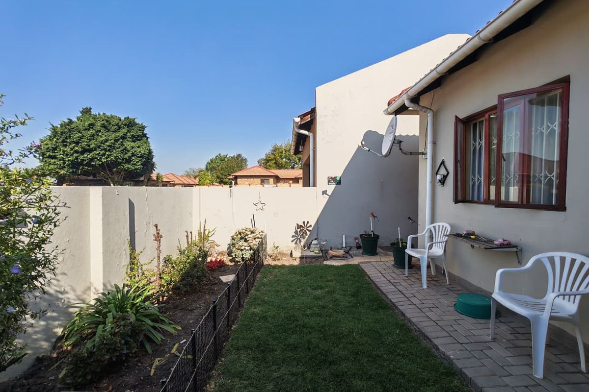 Rear exterior view featuring a paved patio area, small lawn, and boundary wall with visible structural cracking.