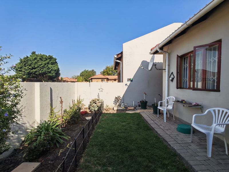 Rear exterior view featuring a paved patio area, small lawn, and boundary wall with visible structural cracking.
