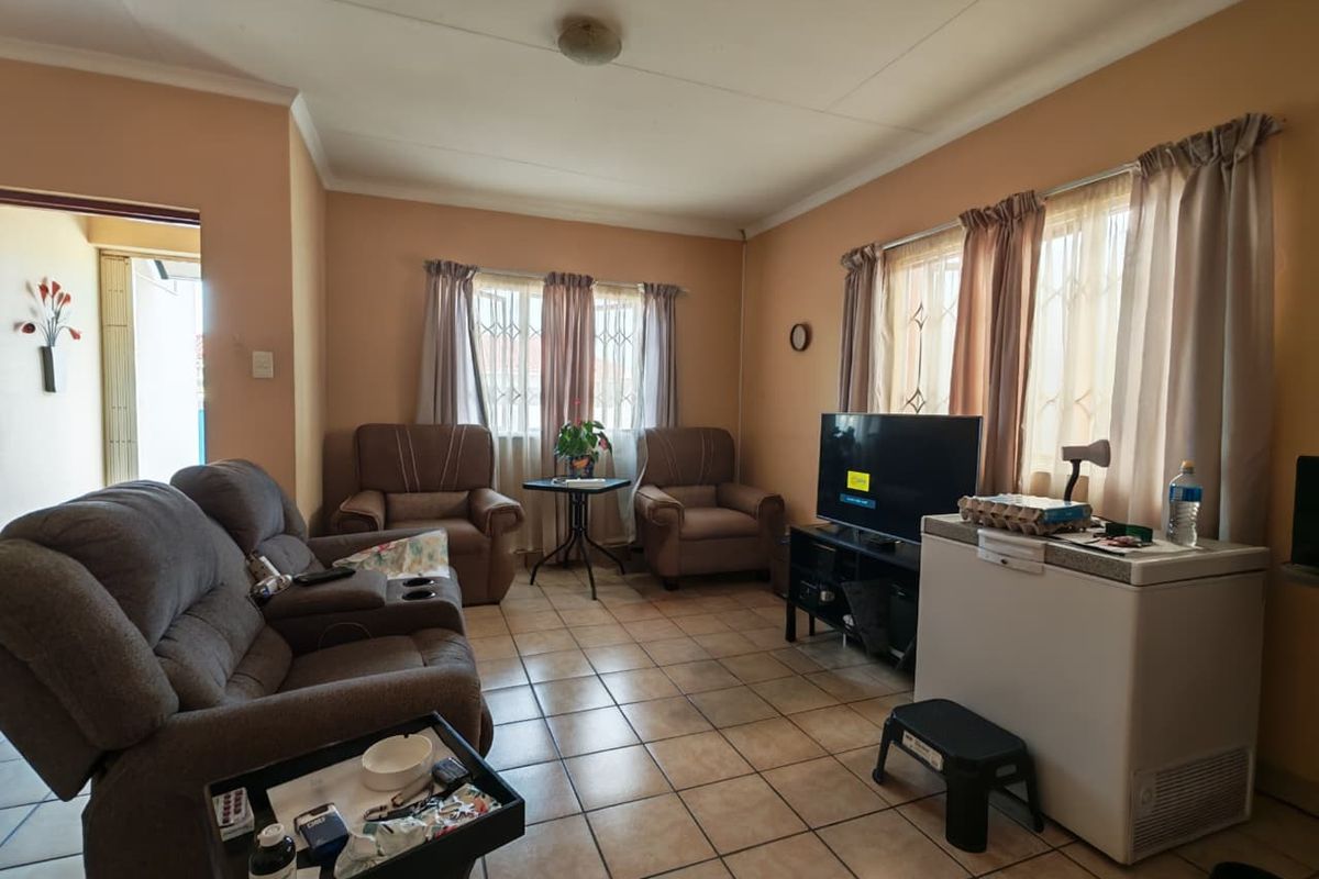 A living room featuring ceramic floor tiles and windows with security bars, offering a functional space with potential for cosmetic updates.
