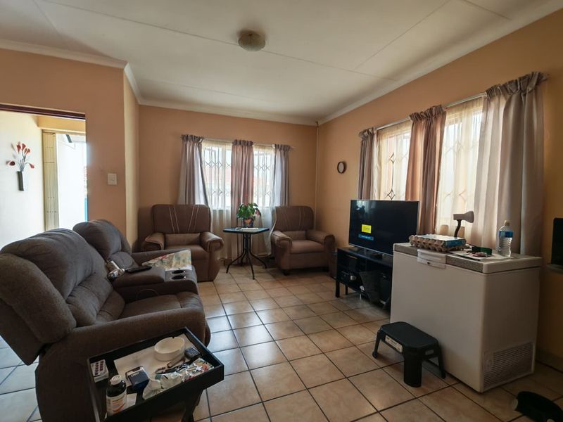 A living room featuring ceramic floor tiles and windows with security bars, offering a functional space with potential for cosmetic updates.