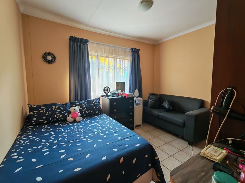 A functional bedroom featuring tiled flooring and a window fitted with a security gate, offering a practical living space.