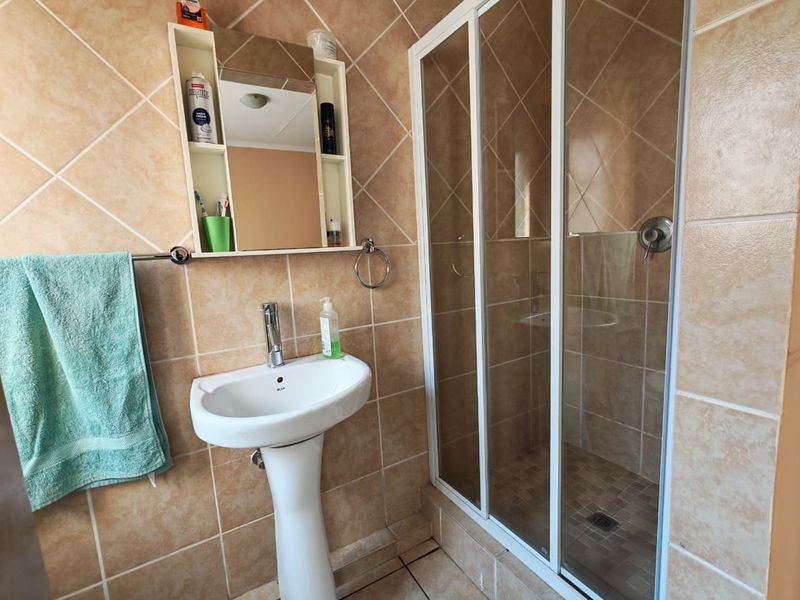 A functional bathroom featuring a pedestal basin, a glass-enclosed shower, and neutral wall tiling throughout.