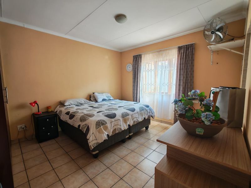 A bedroom featuring tiled flooring, a wall-mounted fan, and security gates on the window. The room requires cosmetic updates to improve its overall condition.