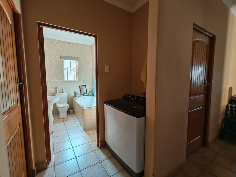 A hallway view leading into a tiled bathroom featuring a bathtub, pedestal basin, and toilet, with adjacent laundry area access.