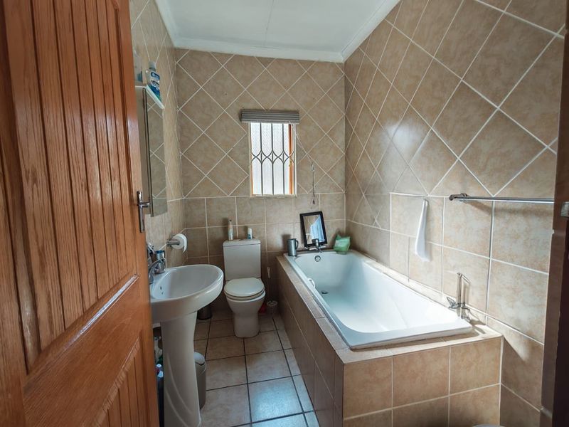 A functional bathroom featuring a pedestal basin, toilet, and a built-in bathtub with full-height ceramic wall tiling.