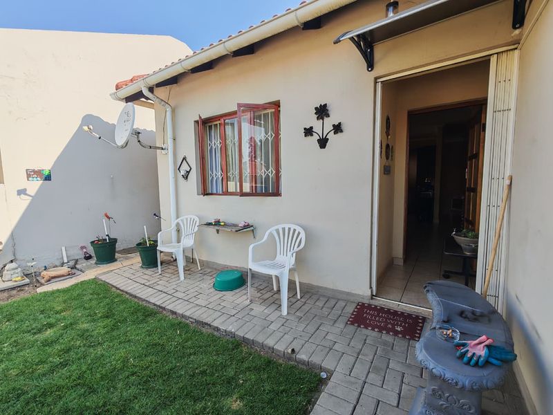 A rear exterior view of the property featuring a paved patio area, small lawn, and direct access into the home.