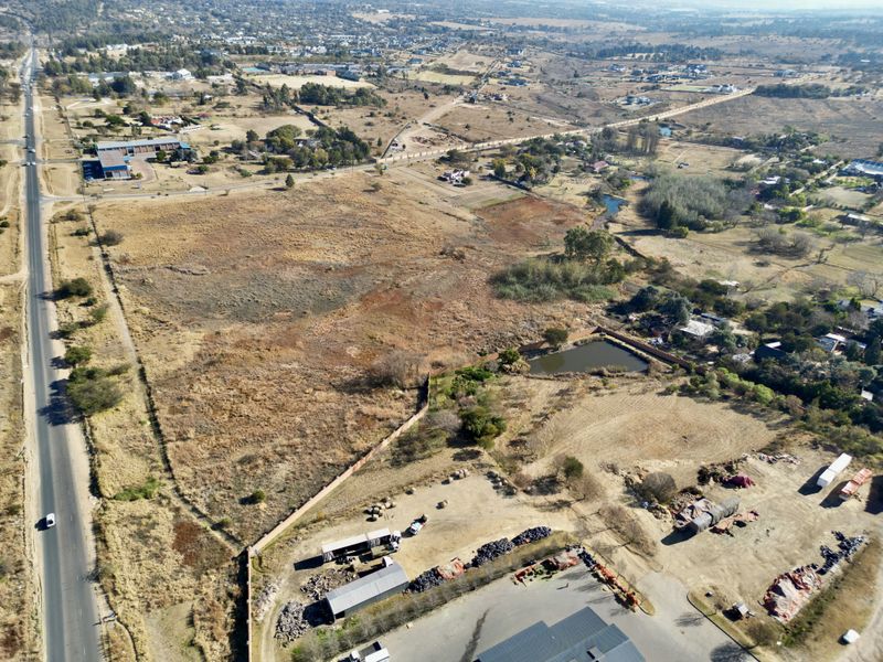 An aerial view of a large vacant residential plot featuring natural landscape, a small dam, and perimeter fencing with adjacent road access.
