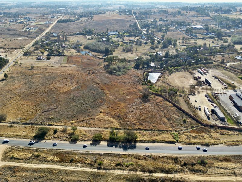 An aerial view of a large, undeveloped residential land parcel featuring natural vegetation and direct access to an adjacent public road.