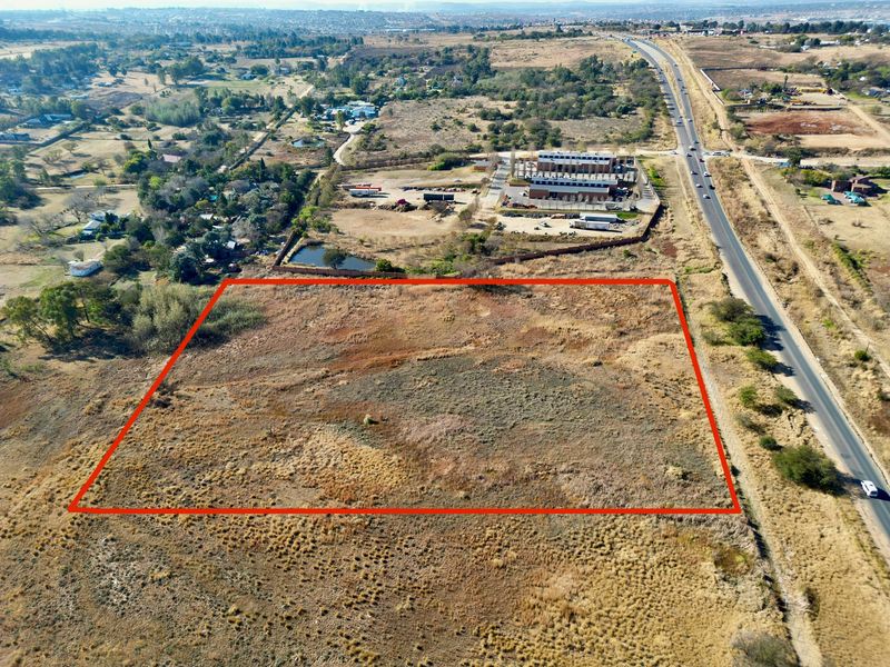 Aerial view of a large, undeveloped vacant residential plot with clear boundary markings, situated near a main road and local infrastructure.