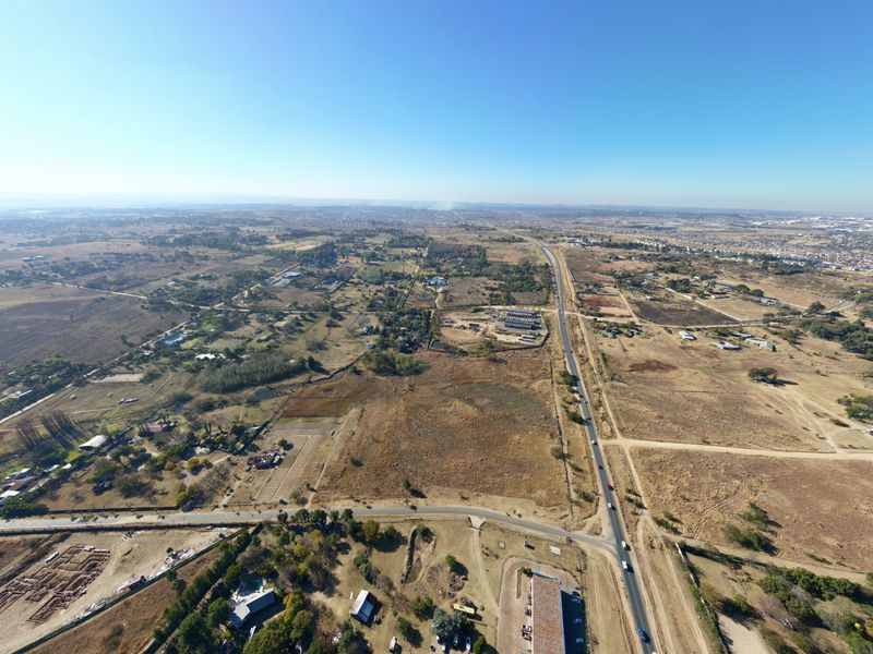 An aerial view of a large expanse of vacant residential land situated adjacent to a main road in a developing area.