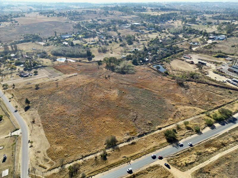 An aerial view of a large, undeveloped residential land plot situated near local roads and surrounding rural landscape.