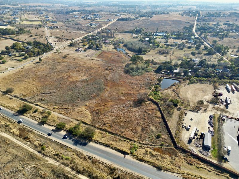 Aerial view of a large, undeveloped vacant land parcel situated near a main road, featuring natural vegetation and a small dam.