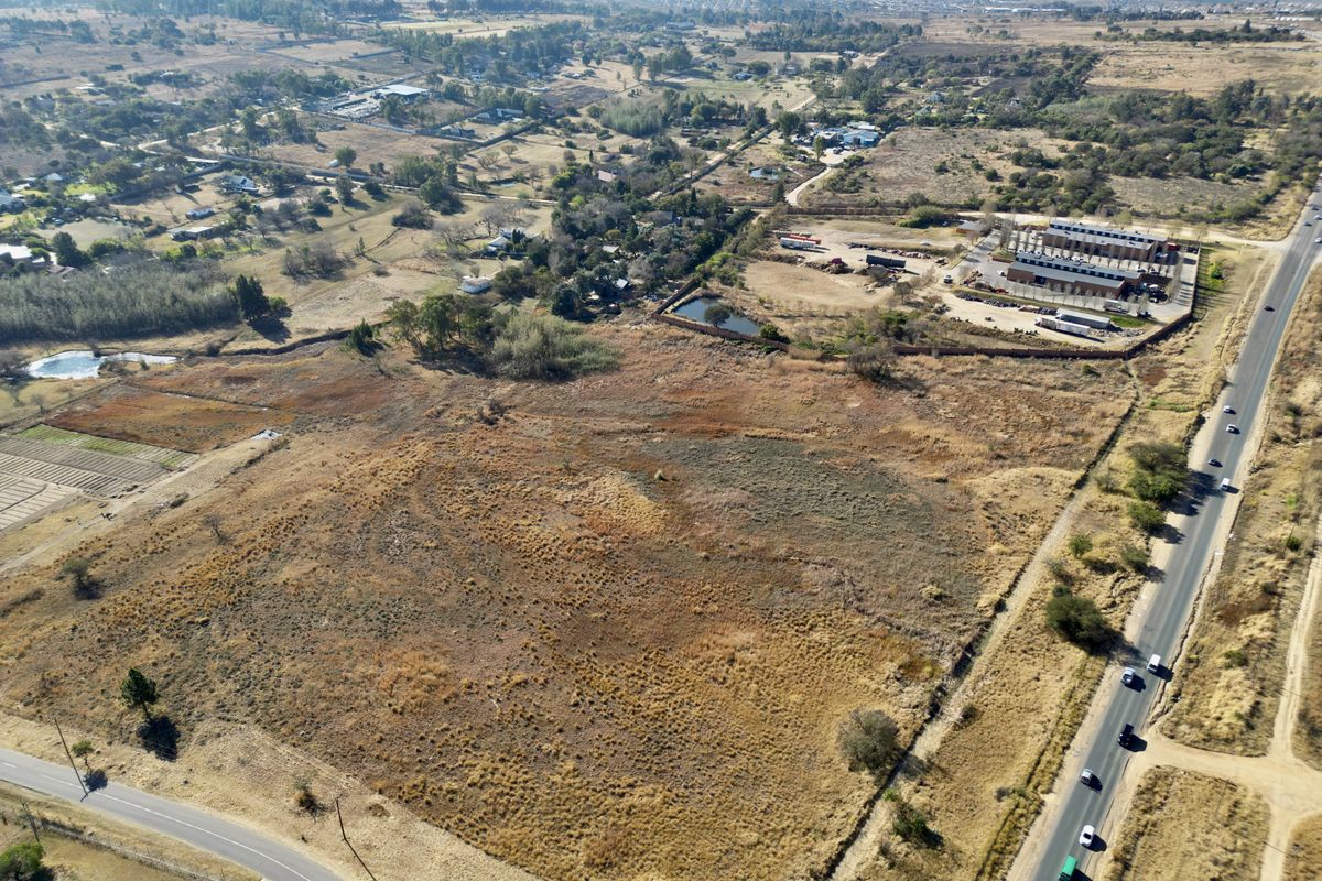Aerial view of a large, undeveloped residential vacant land plot with direct road access and surrounding rural landscape.