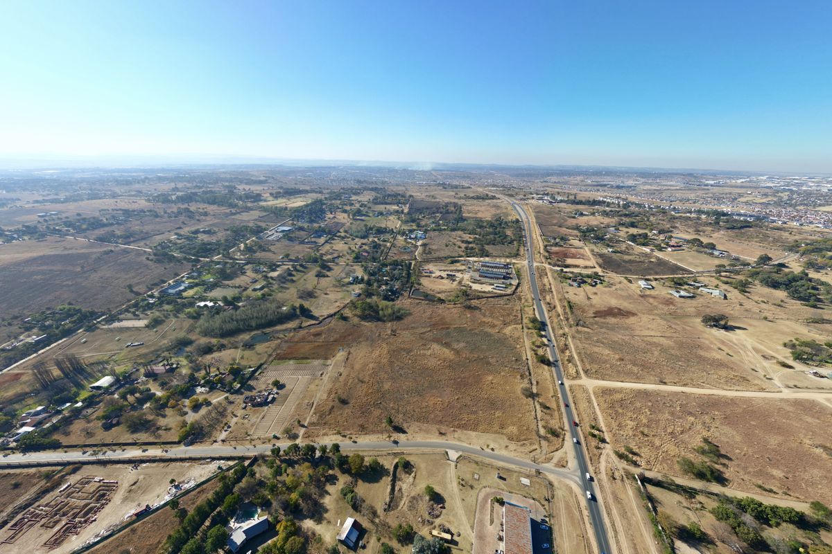 An aerial view of a large expanse of vacant residential land situated adjacent to a main road in a developing area.