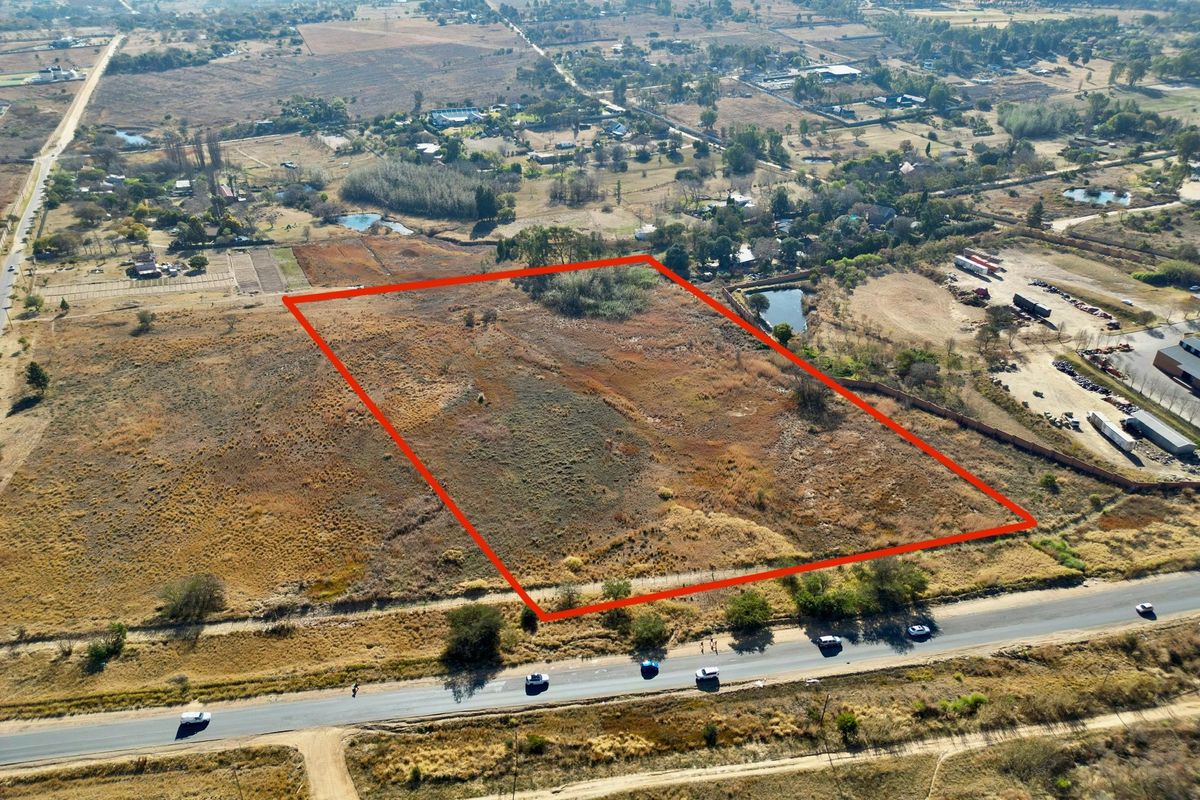 Aerial view of a large, vacant residential plot of land with clear boundary markings, situated in a semi-rural area.