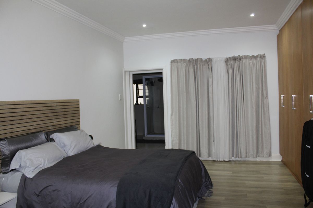 A well-maintained bedroom featuring laminate flooring, built-in cupboards, recessed downlighting, and an en-suite bathroom access.