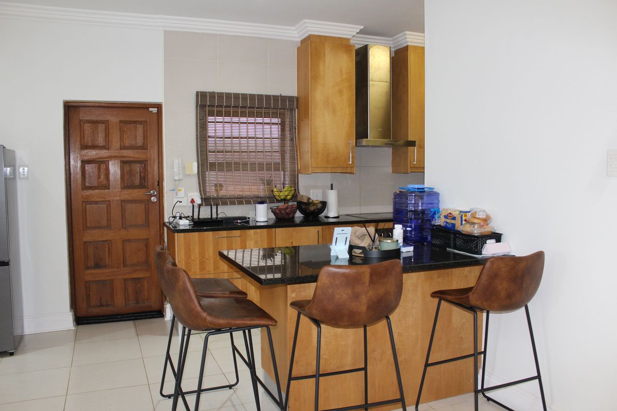 Compact kitchen featuring wooden cabinetry, granite countertops, and a stainless steel extractor fan, complemented by tiled flooring and a solid wood door.