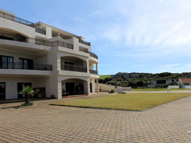 Rear view of a multi-story apartment complex featuring private balconies, paved driveway area, and well-maintained communal lawn space.