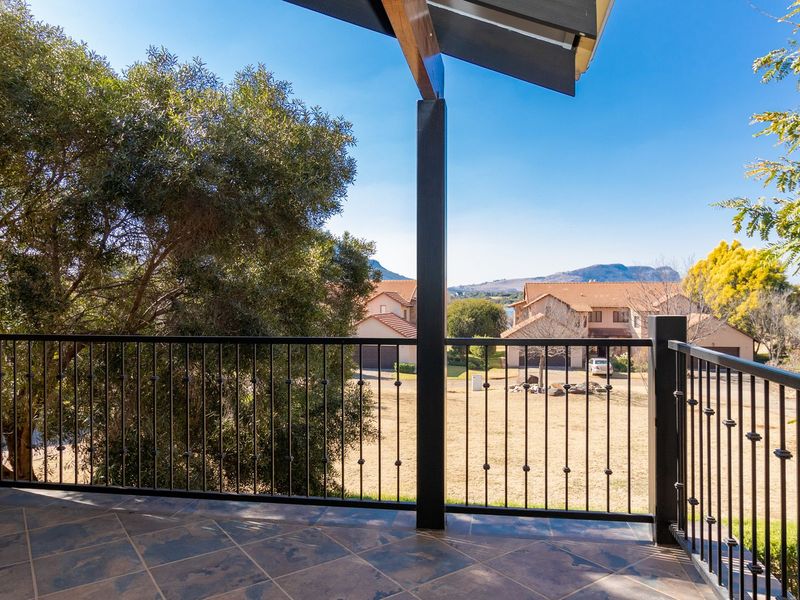 A spacious covered balcony featuring tiled flooring, wrought iron railings, and stone cladding, offering pleasant views of the surrounding neighborhood and landscape.