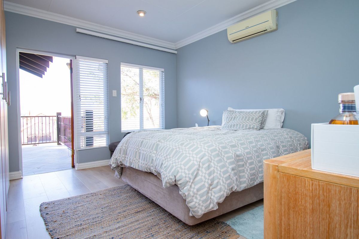A well-maintained bedroom featuring laminate flooring, built-in cabinetry, air conditioning, and direct access to a private balcony through a glass door.