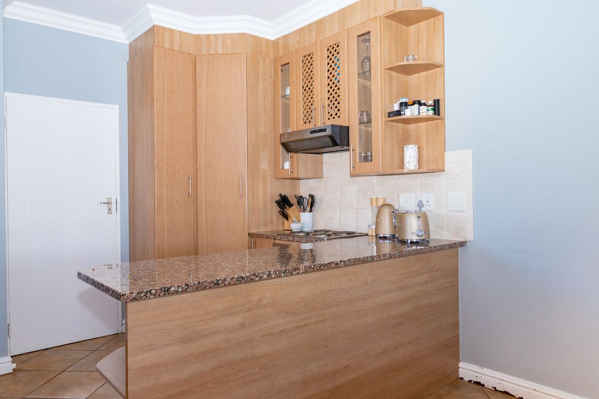 A compact kitchen featuring light wood cabinetry, granite countertops, a built-in hob with extractor fan, and a tiled backsplash.
