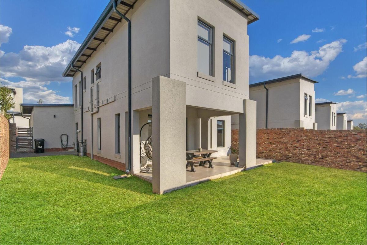 Rear view of a modern double-story townhouse featuring a covered patio, paved area, and a well-maintained private garden with brick boundary walls.