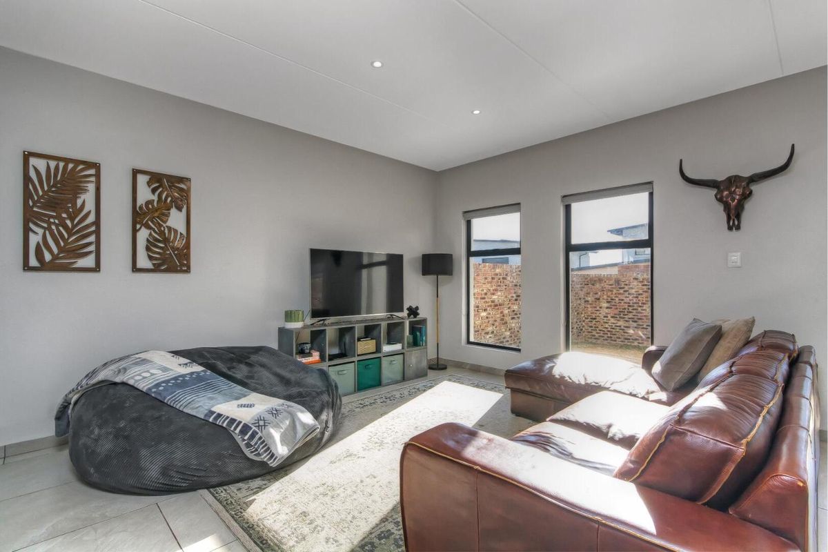 A bright and modern living room featuring large windows with black frames, recessed ceiling lighting, and neutral tiled flooring.