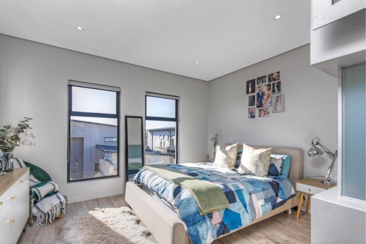 A bright and modern bedroom featuring large windows, recessed ceiling lighting, and light-toned wood-look flooring.