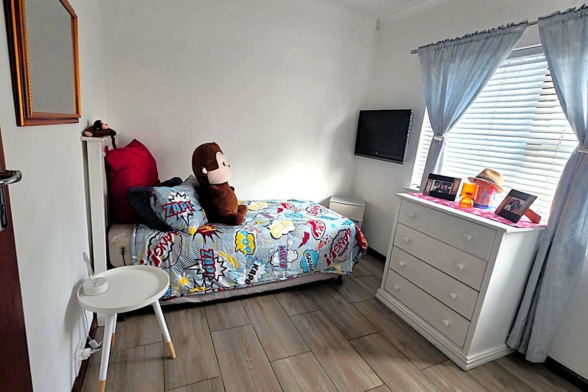 A compact bedroom featuring tiled flooring, neutral walls, and a window fitted with venetian blinds.