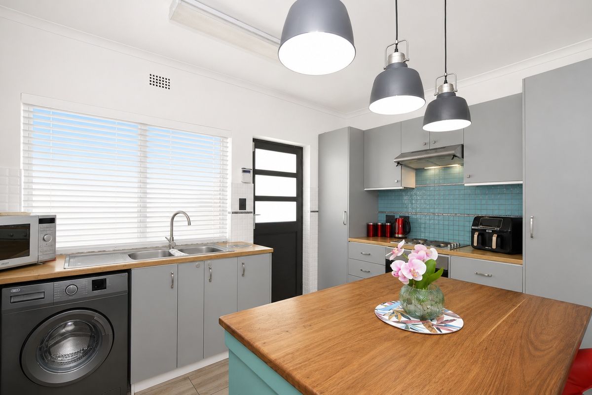 Modern kitchen featuring grey cabinetry, timber countertops, a tiled splashback, integrated laundry space, and stylish pendant lighting.