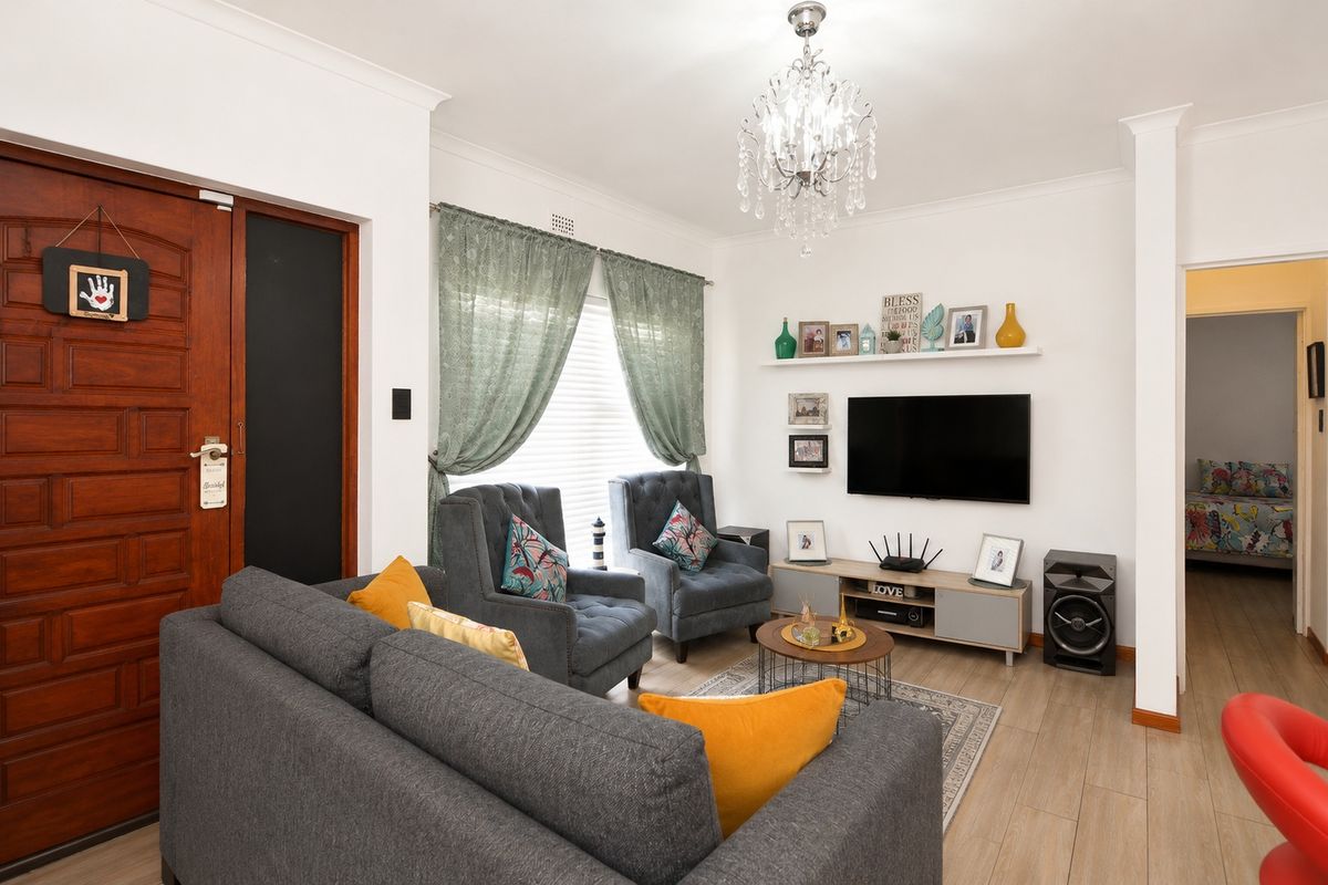 A well-maintained living room featuring laminate flooring, a decorative crystal chandelier, and a wall-mounted television setup with a floating shelf.