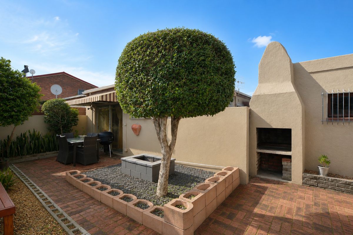 A private rear courtyard featuring a paved patio, a built-in braai, and a landscaped garden area with a central tree.