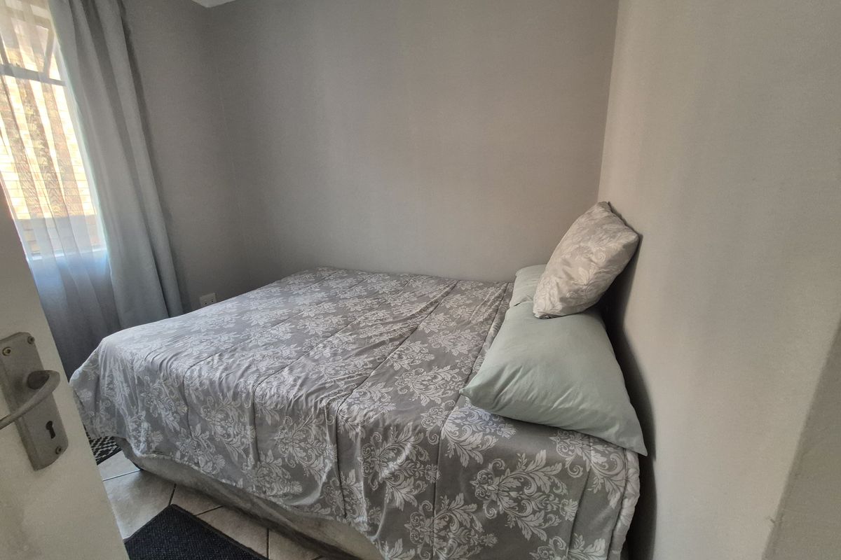A compact bedroom featuring tiled flooring and a window with curtaining, providing a functional and neutral living space.