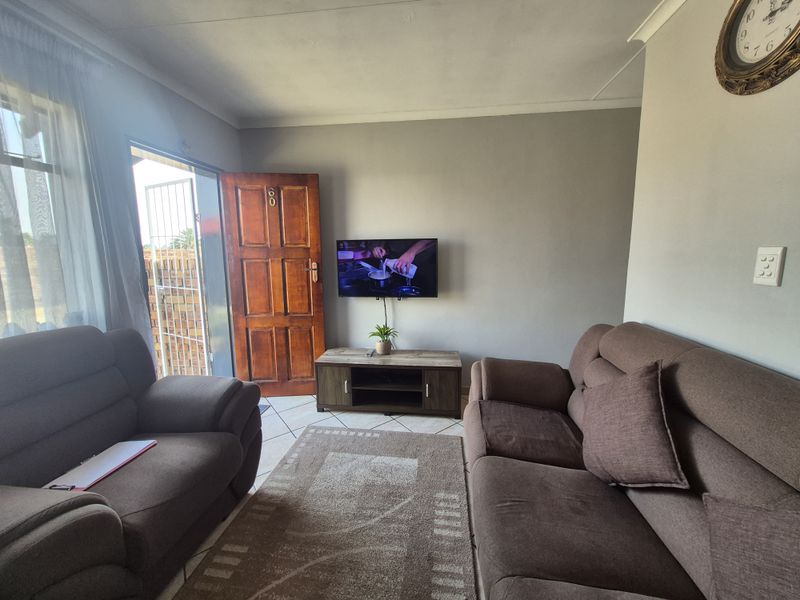A functional living room featuring tiled flooring, a solid timber entrance door, and direct access to the exterior.